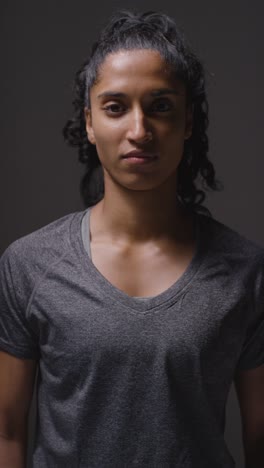 Vertical-Video-Studio-Shot-Of-Woman-Wearing-Sports-Clothing-Against-Dark-Background-Warming-Up